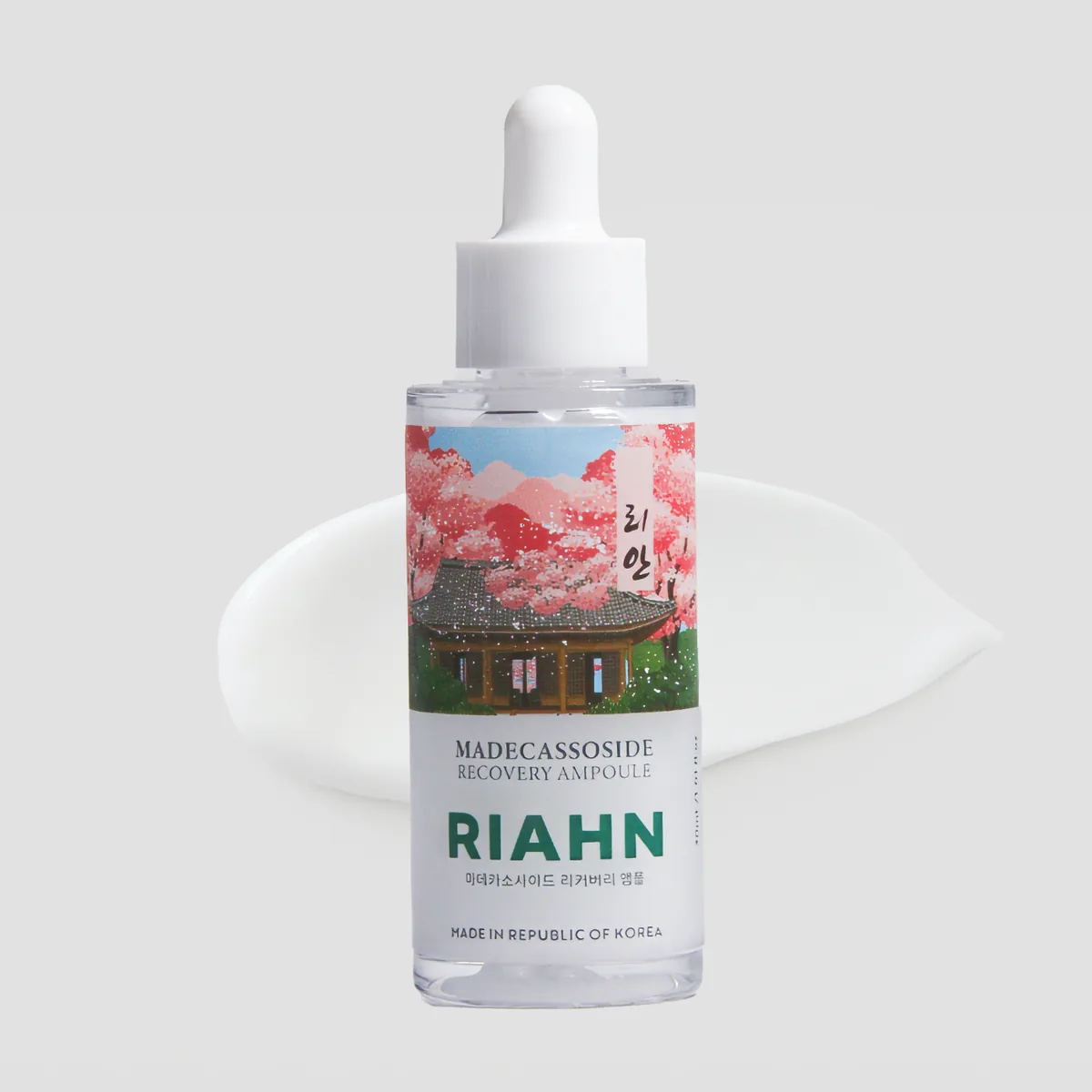 Madecassoside Ampoule: a glass dropper bottle over a smear of white gel, its pink blossom label art behind it.