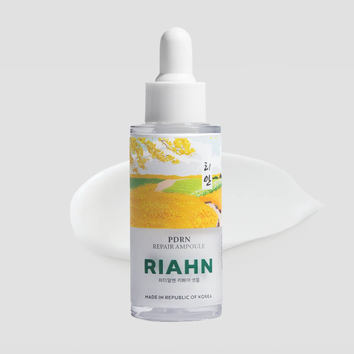 PDRN Ampoule: a glass dropper bottle in front of a soft smear of cream, its golden field label art behind it.